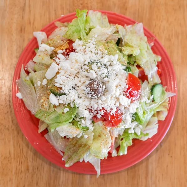 A vibrant salad with lettuce, tomatoes, cucumbers, feta cheese, and a single olive on a red plate.