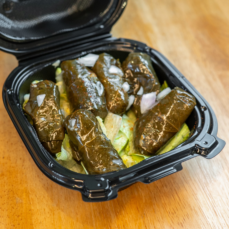 Glazed stuffed grape leaves with visible onion pieces served over lettuce in an open black takeout container.
