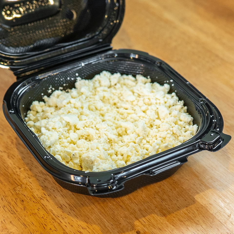 Open black takeout container filled with crumbly pale yellow food on a wooden table.