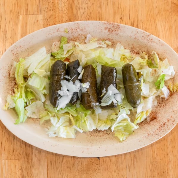 Five dolmas with chopped onions on a bed of shredded lettuce, sprinkled with spices.