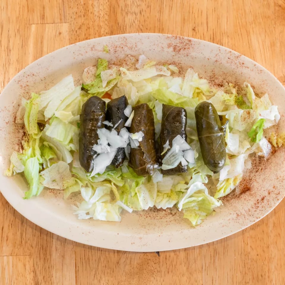 Five dolmas with chopped onions on a bed of shredded lettuce, sprinkled with spices.
