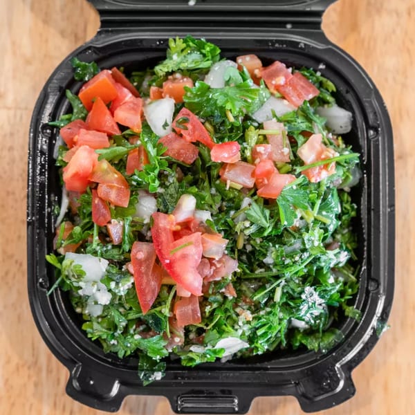 Tabbouleh salad with chopped parsley, tomatoes, and onions in a black takeout container.